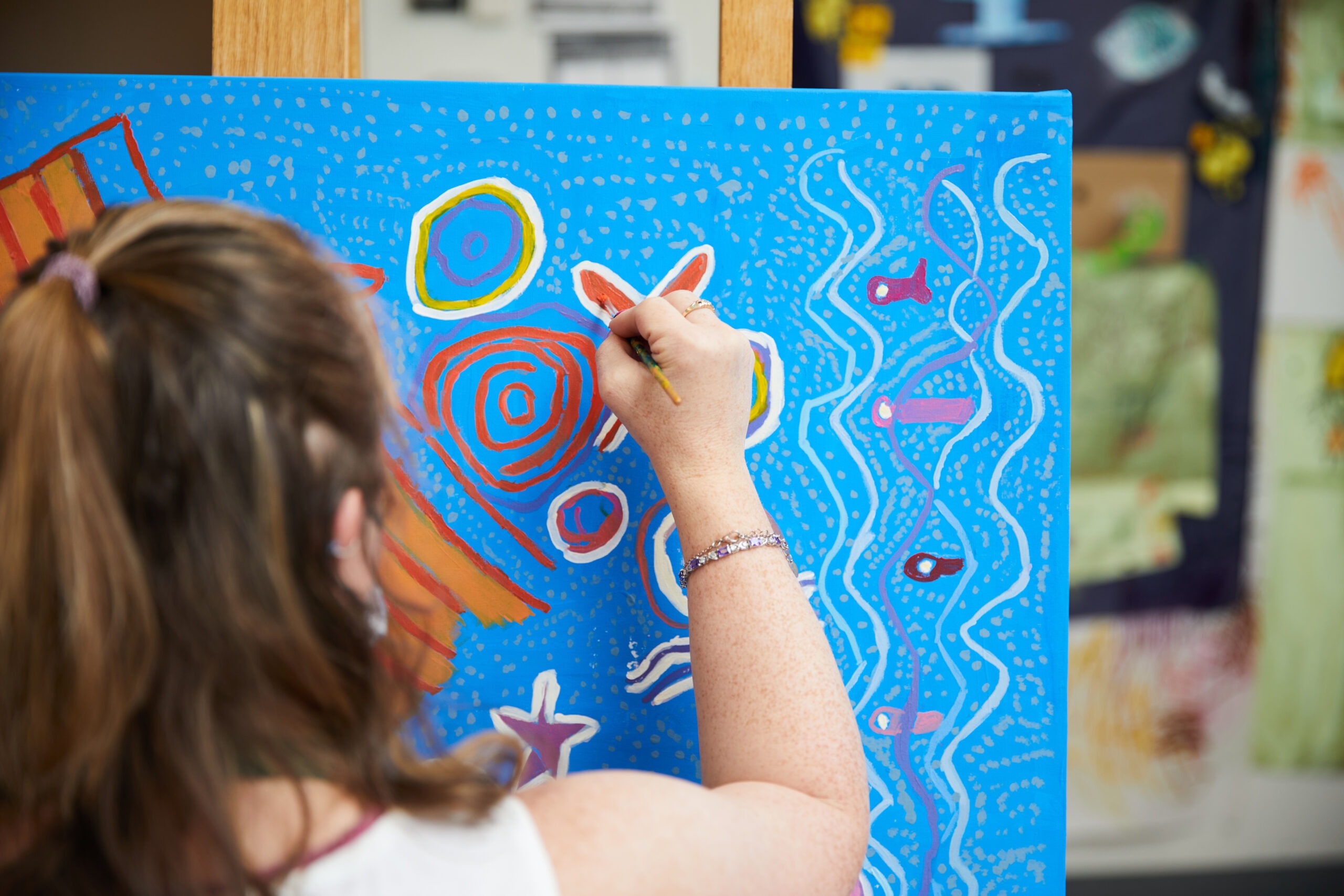 Artist painting a white stroke on a blue canvas.