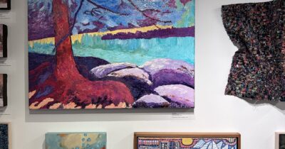 A photo a variety of paintings hung on a blank wall.